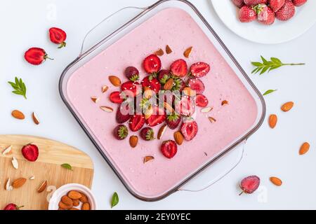 Vue de dessus de cheesecake maison avec fraises et baies et amandes dans un plat en verre sur une table blanche Banque D'Images