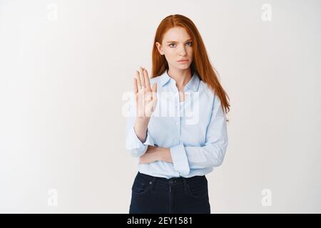 Femme d'affaires sérieuse avec de longs cheveux rouges disant d'arrêter, montrant le signe de rejet et de frowning déçu, dislke et désapprouver quelque chose, blanc Banque D'Images