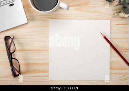 Carte en papier avec vue sur le dessus sur la maquette du bureau. Papier vierge sur fond de bureau en bois. bureau avec feuille de papier vierge, ordinateur portable, fournitures d'écriture et leav vert Banque D'Images