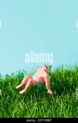 gros plan d'un homme miniature en maillot de bain reposant sur l'herbe, sur un fond bleu avec un peu d'espace sur le dessus Banque D'Images