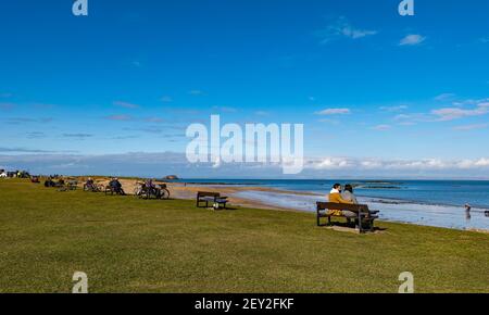 Personnes assises sur des bancs sur la plage en front de mer surplombant Firth of Forth, North Berwick, East Lothian, Écosse, Royaume-Uni Banque D'Images