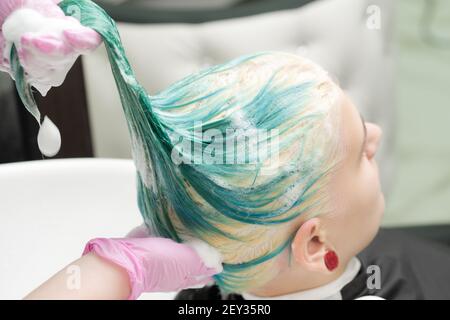 Laver les cheveux verts couleur de la jeune femme avec shampooing dans l'évier. Coiffeur de travail avec gants de protection roses dans un salon de beauté. Banque D'Images