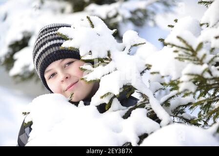 Teen boy a l'air de derrière les arbres en forêt d'hiver Banque D'Images