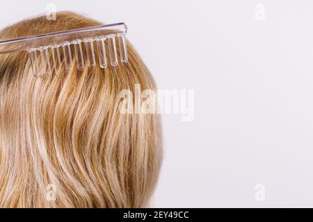 Soins capillaires. Darsonval en forme de peigne et les cheveux blonde de fille de femme. Arrière-plan avec espace latéral pour le texte ou la publicité. Banque D'Images