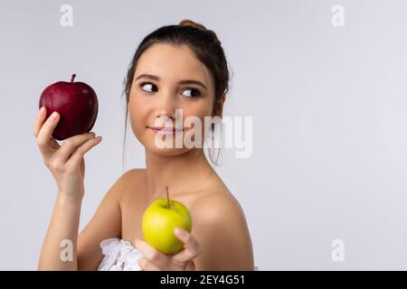 Une jolie brunette enveloppée dans une serviette blanche tient les pommes dans ses mains et regarde sur le côté. Arrière-plan du studio. Espace publicitaire latéral. Banque D'Images