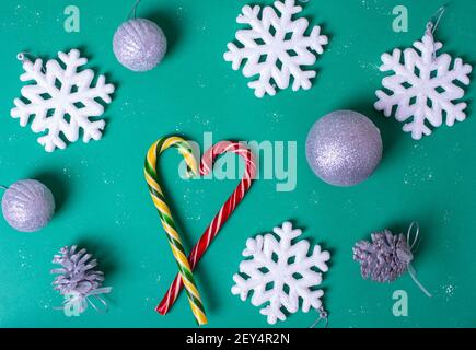 Forme de coeur avec Cannes de Noël, gros flocons de neige blancs, boules argentées sur fond vert, vue du dessus. Peut être utilisé comme carte postale ou comme arrière-plan Banque D'Images