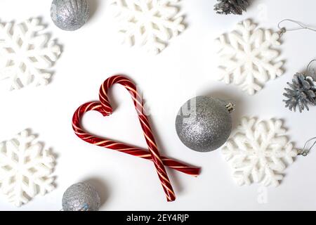 Forme de coeur avec des cannes rouges de Noël, de grands flocons de neige blancs, des boules argentées sur fond blanc, vue du dessus. Peut être utilisé comme carte postale ou rétrogr Banque D'Images