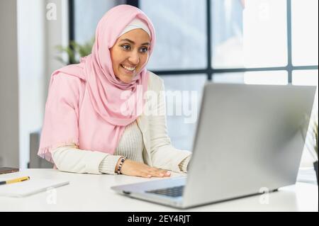 Femme gaie du Moyen-Orient portant un hijab national à l'aide d'un ordinateur portable pour le travail au bureau. Concept de divers employés de bureau, équipe d'affaires multiraciale Banque D'Images