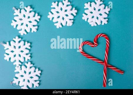 Forme de coeur avec des cannes rouges de Noël, de grands flocons de neige blancs, des boules argentées sur fond bleu, vue du dessus. Banque D'Images