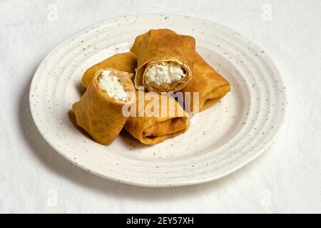 Crêpes françaises fraîches ou blinis russes farcis avec du fromage cottage doux et frais. Assiette blanche sur nappe textile blanc cassé. Banque D'Images