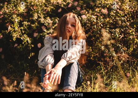 Adolescente assise au milieu de fleurs dans le parc d'été pendant le soleil jour Banque D'Images