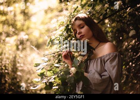 Jeune femme paisible debout par des branches fleuries dans le parc à été Banque D'Images