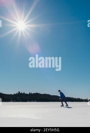 Un jeune garçon patinait sur un lac gelé au Canada par une belle journée d'hiver. Banque D'Images