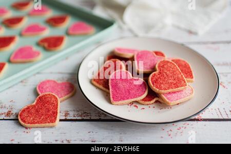 Assiette de biscuits rouges et roses en forme de coeur sur fond de bois blanc. Banque D'Images