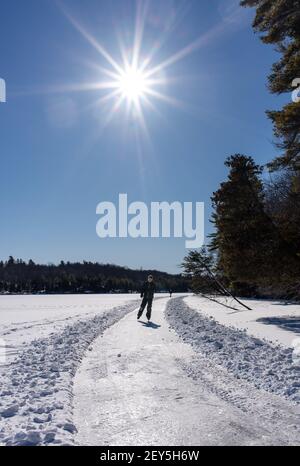 Un jeune garçon patinait sur un lac gelé au Canada par une belle journée d'hiver. Banque D'Images