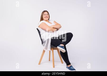 Portrait complet de femme souriante et de taille plus décontractée costume blanc et noir sur chaise noire arrière-plan gris Banque D'Images