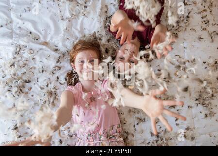 Deux jeunes filles heureuses ayant un oreiller en plumes se battent sur le lit. Banque D'Images