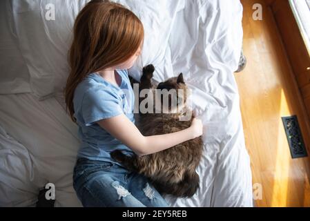 Jeune fille à cheveux bleus heureux rouge sur un lit blanc avec chat. Banque D'Images