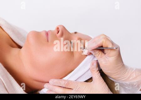 Une photo agrandie d'une femme âgée dans le salon. Les mains de l'esthéticienne plient les sourcils. Concept de beauté. Arrière-plan blanc. Banque D'Images