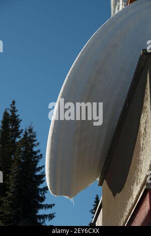 couches de charge de neige suspendues à la maison ou au toit du chalet de ski surplombant la dérive de neige de la fonte gel températures de dégel dangereux entretien de toit d'hiver Banque D'Images