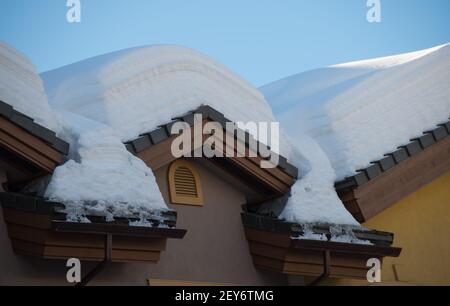 Charge de neige sur le toit d'un chalet de ski à l'architecture européenne en hiver, après la tempête de neige à la station de ski, la neige a fondu et dégelé le fond bleu du ciel Banque D'Images