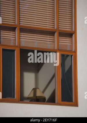 stores ou abat-jour marron bloquant la lumière qui traverse l'extérieur la lumière de la fenêtre d'accueil encadrée en bois projette des ombres sur le mur antérieur maison sof et lampe Banque D'Images