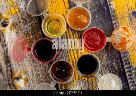 Vue de dessus sur six sauces et marinades colorées douces et épicées remplies à l'intérieur des bols en plastique sur une table en bois abîmé. Banque D'Images