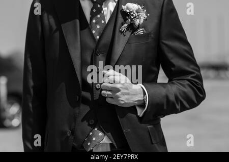 Le matin, le marié dans une veste, le marié redresse le boutonnière, le jour du mariage. Mariage. Détails. Photo en noir et blanc Banque D'Images