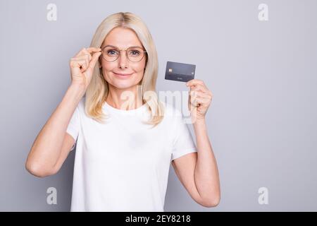 Photo portrait d'une vieille dame tenant une carte de crédit isolé à la main sur fond gris Banque D'Images