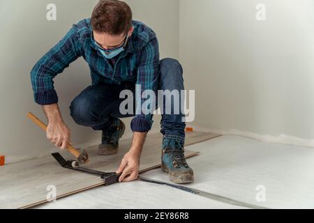 homme avec masque d'installation d'un plancher en bois avec des outils pour son installation Banque D'Images