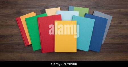 Vue de haut en bas d'une pile de livres colorés et lumineux centrés sur un bureau sombre. Banque D'Images