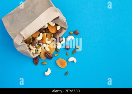 Mélange de différents noix et abricots séchés dans un sac en papier sur fond bleu. En-cas sain. Pour afficher. Copier l'espace. Banque D'Images