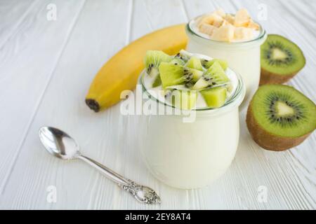 Yaourt au lait naturel avec kiwi et banane dans les pots en verre sur fond de bois blanc. Gros plan. Banque D'Images