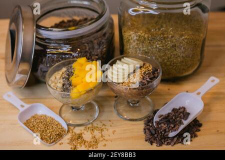 Deux bols d'ingrédients sains pour le petit déjeuner; pots en verre avec grains de cacao et graines de lin en arrière-plan Banque D'Images