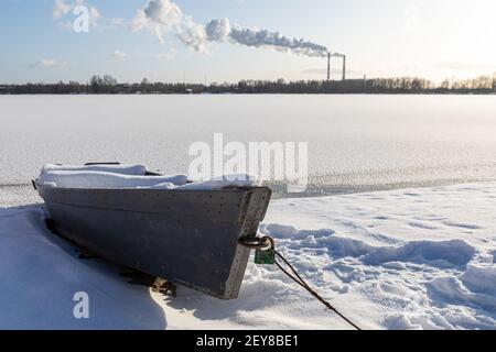 Vieux bateau à rames en bois recouvert de neige sur la rive en hiver. Bateau de pêche. Un lac ou une rivière gelé. Température ambiante basse. La saison de l'hiver Banque D'Images