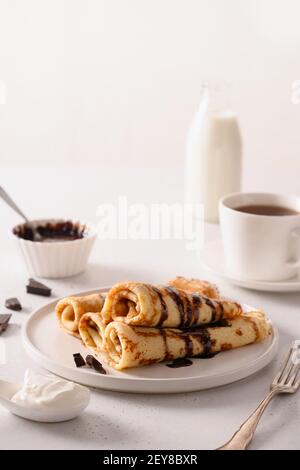 Crêpes fines avec du chocolat et de la crème aigre comme des rouleaux sur le blanc. Petit déjeuner traditionnel russe pour Shrovetide. Gros plan. Banque D'Images