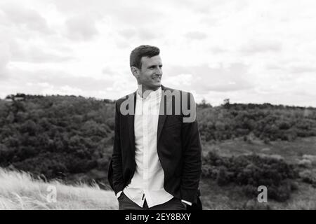 Homme souriant en chemise blanche et veste debout dans la rue avec les mains dans les poches. Homme d'affaires. Portrait d'homme Banque D'Images