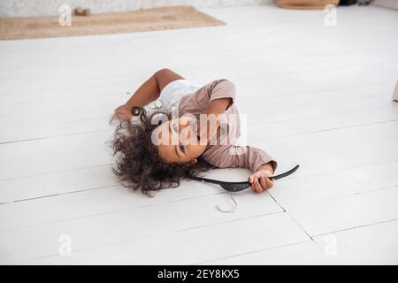 Une petite fille afro-américaine maurique se trouve sur un lit blanc, s'amuse, rit, sourit, joue. Le concept d'adoption d'une famille multiethnique. Balayage minimaliste Banque D'Images