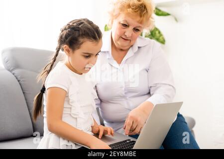 Grand-mère mature aidant l'enfant à faire ses devoirs à la maison. Une vieille grand-mère satisfaite aide sa petite-fille à étudier dans son salon. Petite fille écrivant Banque D'Images