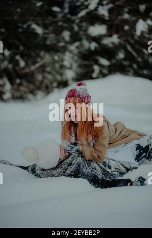 Une belle vue d'une femme aux cheveux de gingembre et de son petit ami riant en tombant dans la neige avec des vêtements complètement couverts de neige Banque D'Images