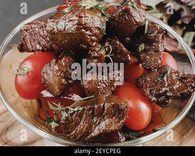 Tranches de boeuf grillé bifteck de contre-filet barbecue et salade de tomates et roquette sur découper close-up Banque D'Images