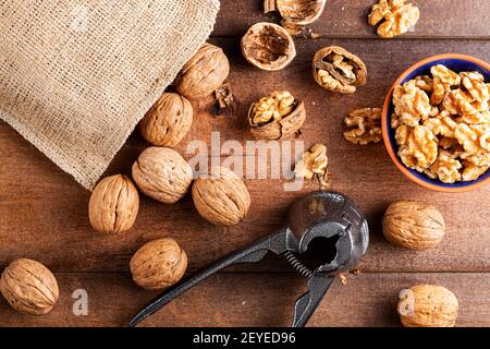 Image plate montrant une pince en noyer en fonte (outil casse-noisette) avec noix fraîches brutes en coque sur table en bois. Un petit bol de noix Banque D'Images