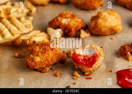 Image rapide et pratique avec mise au point sélective des nuggets de poulet frits en gros morceaux trempés dans du ketchup de tomate rouge sur du papier de cuisson. R Banque D'Images