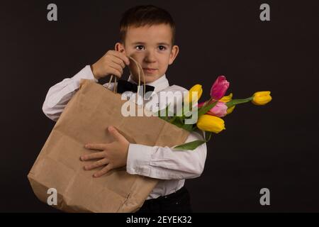 le garçon avec le vitiligo dans une chemise blanche et un Noeud papillon avec tulipes sur fond noir Studio Banque D'Images