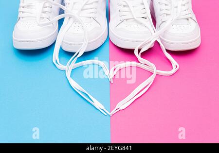 Vue rognée des sneakers blanches assorties et du symbole en forme de coeur des lacets sur fond bleu rose. Concept romantique pour les couples portant des vêtements assortis Banque D'Images