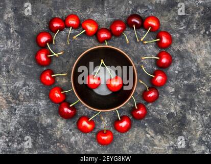 Symbole coeur rouge fait de cerises douces mûres avec un bol au centre sur un fond grundy. Composition romantique de fruits. Banque D'Images