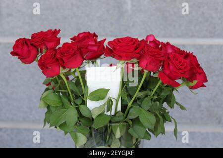 Bouquet de roses rouges dans un vase et une note blanche pour l'écriture d'un message d'accueil. Banque D'Images