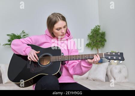 Jeune femme jouant de la guitare acoustique noire, assise à la maison sur un canapé Banque D'Images