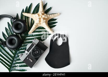 Déplacement à plat. Appareil photo, masque de protection, casque, feuilles tropicales sur fond blanc Banque D'Images