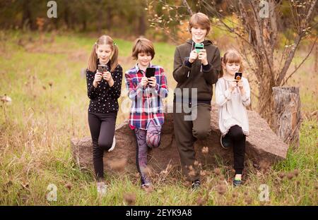 Groupe d'enfants d'école jouant dans le téléphone mobile ensemble pendant en plein air dans le parc d'été Banque D'Images